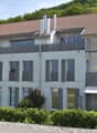 Modern two-story house with white facade, large windows, multiple balconies, and a well-maintained garden.