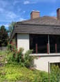 Single-story house with a modern design, featuring a raised ground floor, large windows, and a well-maintained garden with colorful flowers and an umbrella.