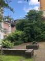 A small, enclosed garden area with gravel pathways, stone benches, and lush greenery, surrounded by residential buildings.