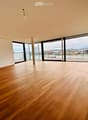 Empty room with wooden flooring, large windows, and a view of a river and cityscape.