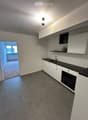 Modern kitchen with white cabinets, black countertop, sink, and oven. Open doorway leads to another room with brick flooring.