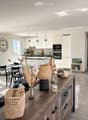 Open-plan living and dining area with modern furniture, large windows, and a kitchen area in the background.