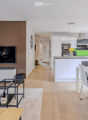 Modern open-plan living and dining area with a sofa, coffee table, TV, and a dining table with chairs. The kitchen features white cabinets, a kitchen island, and various appliances.