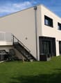 Modern two-story house with a raised ground floor, featuring a balcony, staircase, and outdoor grill area.