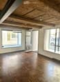 Empty room with wooden flooring, exposed wooden ceiling beams, large windows, and a door leading outside.