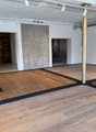 Empty room with wooden flooring, white walls, exposed ceiling beams, and a large wooden door in the background.