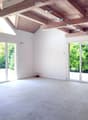 Bright, open room with white walls, exposed wooden ceiling beams, large glass doors leading to outdoor space, and a tiled floor.