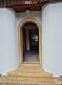 An arched entryway leads into a hallway with white walls and a wooden ceiling. The hallway is empty and has a smooth, light-colored floor.