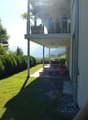 Garden area with a well-maintained lawn, wooden deck, potted plants, and a covered balcony area with outdoor furniture.