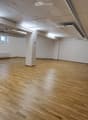 Empty room with wooden flooring, white walls, and exposed ceiling beams. No furniture or equipment present.