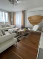 Modern living room with white leather sofas, a coffee table, a small side table, a hanging woven basket, and a decorative sculpture on a console table.