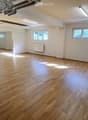 Empty room with wooden flooring, white walls, and large windows allowing natural light. No furniture or equipment present.