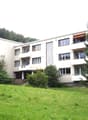 Modern multi-story residential building with balconies, surrounded by greenery and trees.