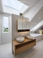 Modern bathroom with two sinks on a wooden vanity, a large mirror with built-in cabinets, a bathtub, and a skylight window providing natural light.