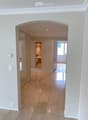 Bright hallway with beige tiled flooring, white walls, and recessed lighting. An open doorway leads to a bathroom with a visible bathtub and a windowed door to the outside.