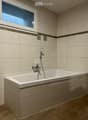 Modern bathroom with a bathtub, faucet, and showerhead. Light-colored tiles and a window provide natural light.
