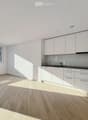 Modern kitchen with white cabinets, light wooden flooring, and a large window offering a view of the street.