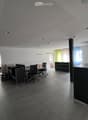 Modern office space with desks, chairs, and cabinets. Tiled floor and white walls. Office equipment and lamps visible.