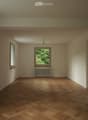 Empty room with wooden herringbone flooring, light-colored walls, and two windows with radiators beneath them.