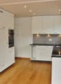 Modern kitchen with white cabinets, wooden flooring, stainless steel sink, and built-in oven.