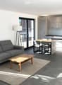 Modern open-plan living and dining area with grey sofa, wooden coffee table, dining table with chairs, and a sleek kitchen with cabinets and a countertop.