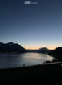 View from a balcony or terrace overlooking a serene lake with distant mountains during sunset.