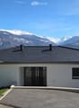 Modern white house, black roof, large windows, driveway, snowy mountains in the background