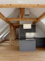 Modern kitchen with wooden beams, light wooden flooring, grey cabinets, and a central island.