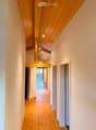Wooden hallway with exposed wooden beams and recessed lighting, leading to an open area with a view of a balcony.