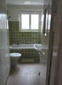 Bathroom with green patterned tiles, bathtub, toilet, sink, and a window above the bathtub.