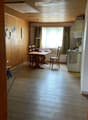 A furnished room with a wooden table and chairs, a kitchen area with a stove and fridge, and wooden walls and flooring.