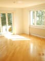 Empty room with light wooden flooring, large windows, and sliding glass doors leading to a balcony.