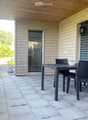 Outdoor patio with a wooden ceiling, tiled floor, and a black wicker dining set including a table and chairs. A sliding glass door leads to the interior, and there are potted plants and greenery nearby.