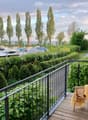 Balcony with wooden decking, metal railing, and a view of a harbor with boats and trees.