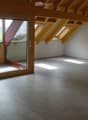 Empty room with exposed wooden beams, tiled floor, large sliding glass door leading to a balcony, and skylights allowing natural light.