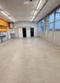 Empty room with white walls, large windows, and a sink area in the corner. No furniture or equipment present.