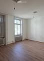 Empty room with wooden flooring, white walls, and large windows with curtains. Radiators are visible beneath the windows.