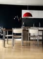 Modern dining area with a wooden table, white chairs, and a sleek kitchen area featuring white cabinets and a red pendant light.