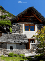 Stone house with wooden doors and windows, situated in a mountainous area with a stone staircase leading to the entrance.