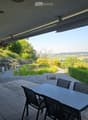 Outdoor patio with tiled floor, table and chairs, grill, and scenic view of greenery and countryside.
