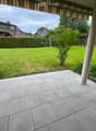 Well-maintained garden with a tiled patio, green lawn, hedge border, and surrounding trees and houses.