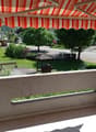 Balcony with tiled floor, stone railing, and striped awning, overlooking a green lawn and residential area.