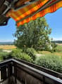 Balcony with wooden railing, striped awning, overlooking a rural landscape with fields, trees, and distant hills.
