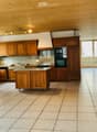 Bright kitchen with wooden cabinets, a central island, and modern appliances including an oven and microwave. Features a tiled floor, large windows, and a wood-burning stove.