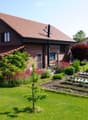 A well-maintained garden with a lawn, flower beds, a small tree, and a patio area with a table and chairs near the house.