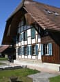 Traditional wooden house, brown roof, blue shutters, chimney, driveway, car parked, garden, wooden fence
