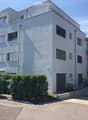 white building, 3 levels, windows with white frames, 2 garages, shrubs and trees in front, entrance on left side