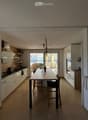 Modern kitchen with white cabinets, a dining table with chairs, and a view through large windows.