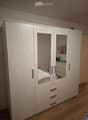 Modern bedroom with large white wardrobe, bed with blue bedding, nightstand, and mirror on the wardrobe door.