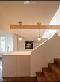 Open kitchen area with light-colored cabinets, wooden staircase, pendant lights, and large windows allowing natural light.